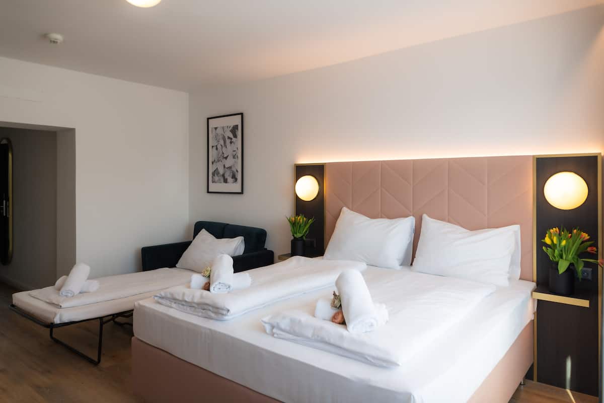 A hotel room with two beds, a desk, and a chair. There are towels on the beds and a vase with flowers on the desk.