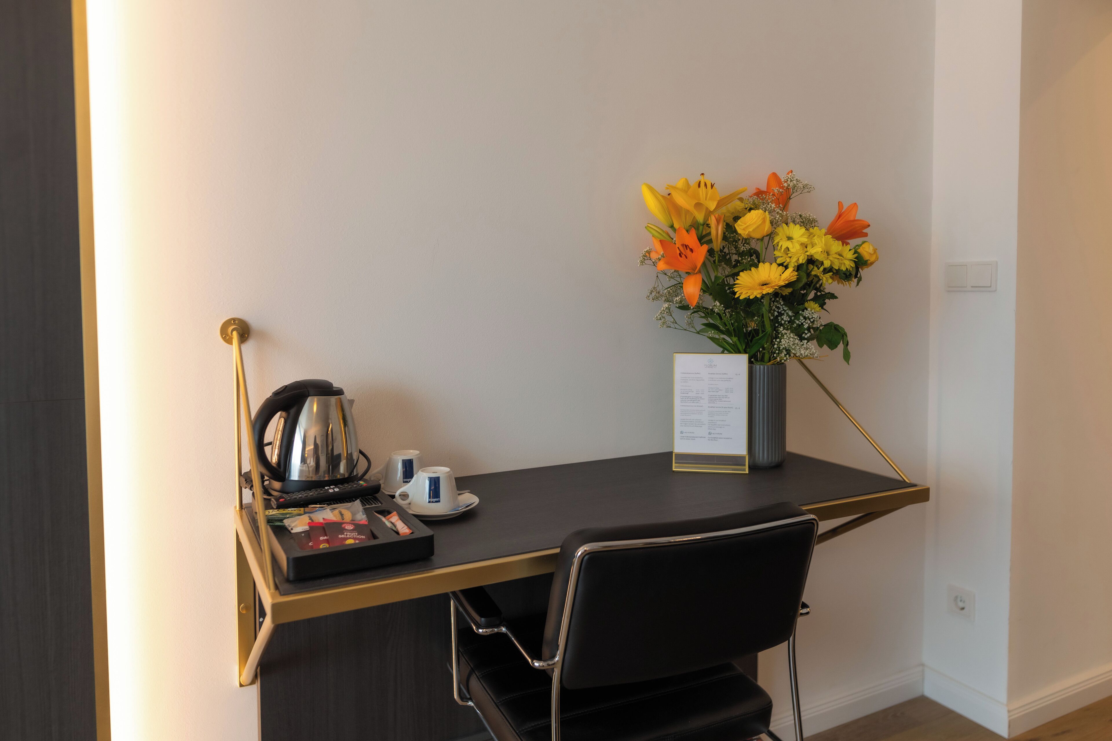 Une chambre d’hôtel équipée d’un bureau, d’une machine à café, d’un vase avec des fleurs et d’un menu posé sur la table.