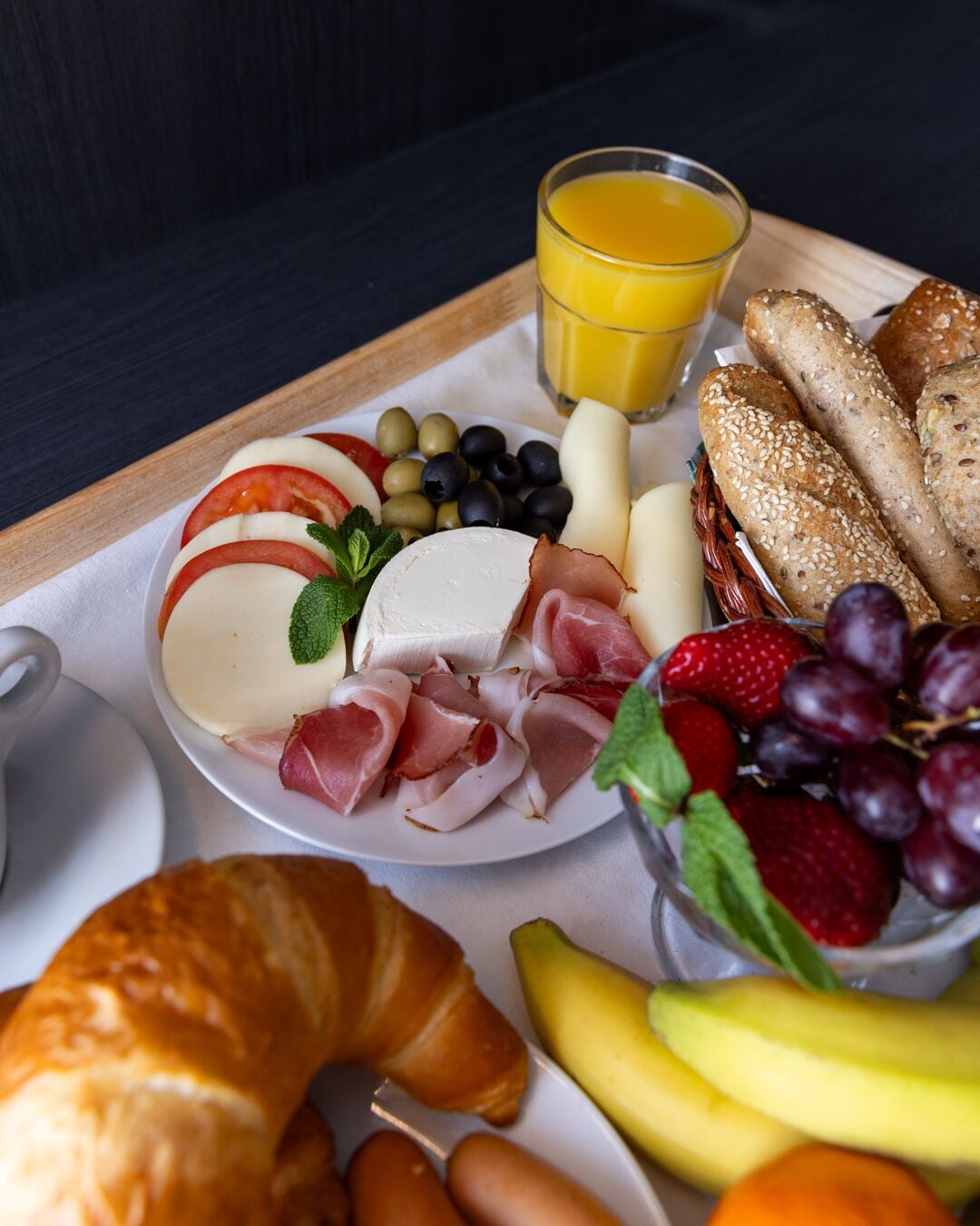 A breakfast tray with cheese, ham, grapes, strawberries, and a croissant.