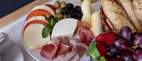 A breakfast tray with cheese, ham, grapes, strawberries, and a croissant.