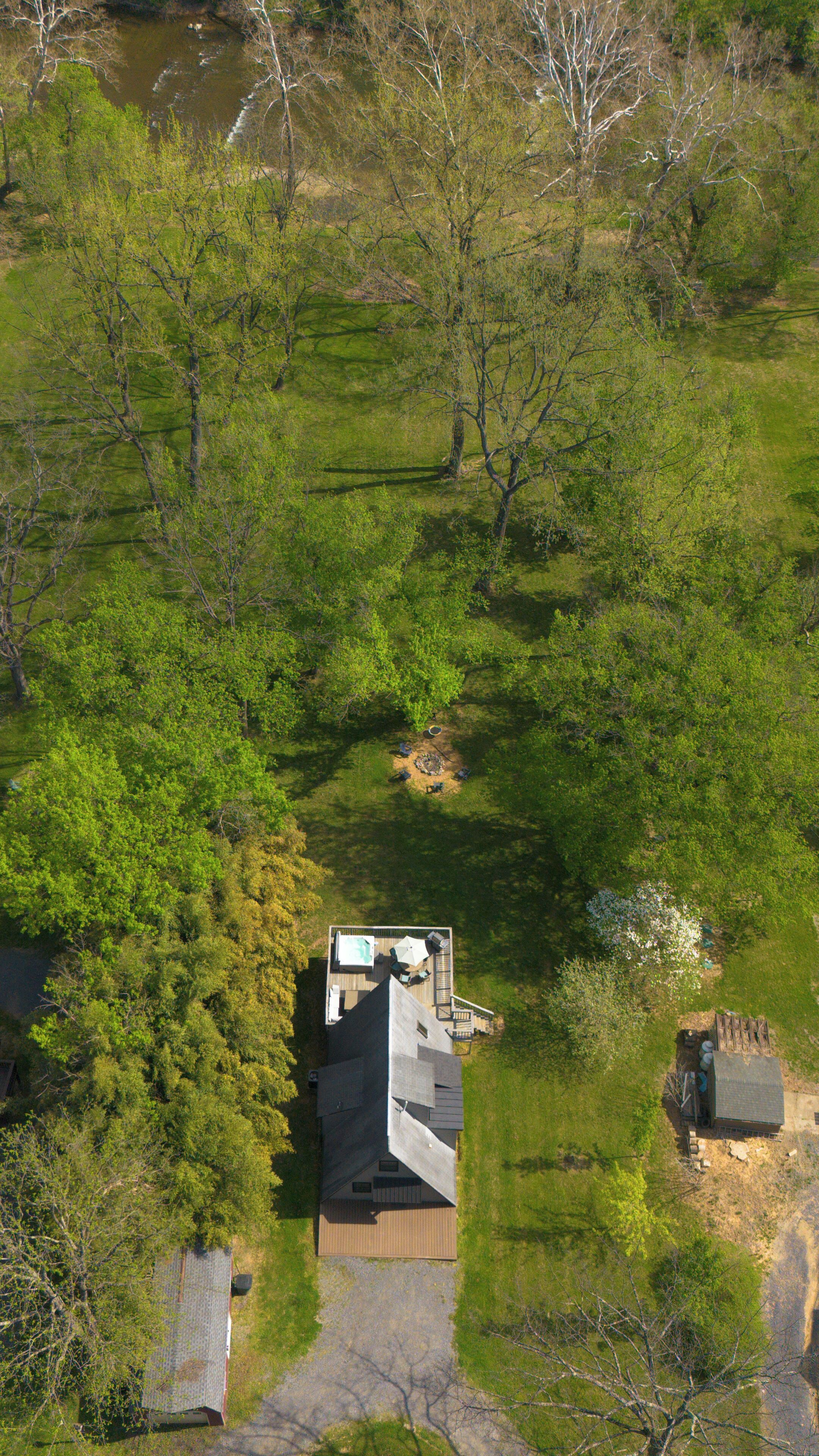 Vue aérienne d’une maison dotée d’une terrasse, entourée d’une végétation luxuriante et d’arbres.