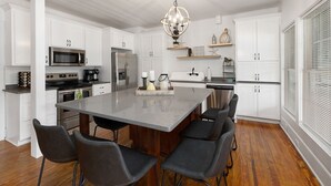 Una cocina moderna con armarios blancos, electrodomésticos de acero inoxidable, una isla grande con taburetes de bar y un candelabro decorativo.