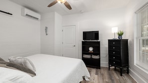 Un dormitorio con cama, televisor, cómoda y ventana con persianas.