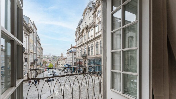 A view from a window overlooking a cobblestone street with historic buildings, a metal railing, and a clear sky.