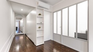 A hallway with a white built-in shelving unit, a large window with a view, and a wooden floor.