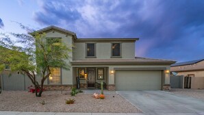 A two-story house with a front porch, a garage, and a landscaped front yard with a small tree and shrubs. - Pool & Patio: Family-Friendly Goodyear Home! (Goodyear)