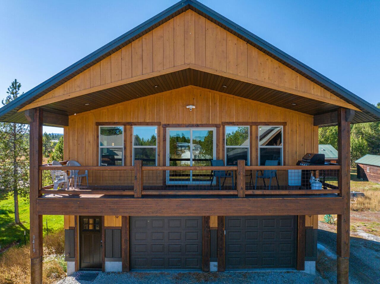 Une cabane en bois à deux étages, dotée d’un balcon, de grandes fenêtres et d’un garage.
