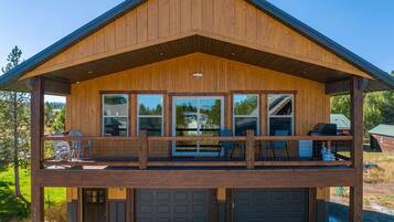 Une cabane en bois à deux étages, dotée d’un balcon, de grandes fenêtres et d’un garage.