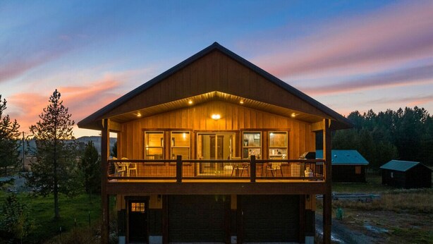 A two-story wooden cabin with a balcony, large windows, and a garage.