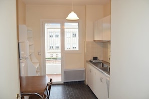 A compact kitchen with a dining area, a window with a view of buildings, and a hanging light fixture. - Apartment for 6 in a standing residence with swimming pool (CAVALAIRE sur mer)