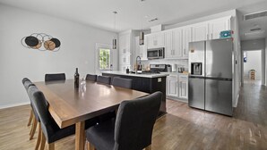 A modern kitchen with white cabinets, stainless steel appliances, and a wooden dining table with chairs. - Budget-Friendly Retreat Stockyards HotTub MiniGolf (Fort Worth)