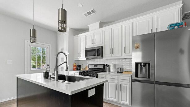 A modern kitchen with white cabinets, stainless steel appliances, and a large island with a sink. - Budget-Friendly Retreat Stockyards HotTub MiniGolf (Fort Worth)