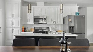 A modern kitchen with white cabinetry, stainless steel appliances, and a dining area with a dark wooden table and chairs. - Budget-Friendly Retreat Stockyards HotTub MiniGolf (Fort Worth)
