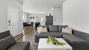 A modern living room with a grey sofa, white coffee table, and a dining area in the background. - Budget-Friendly Retreat Stockyards HotTub MiniGolf (Fort Worth)