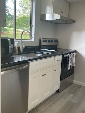 Enjoy cooking in this kitchen with a stainless steel range hood, dishwasher, oven, and microwave, and a window offering a view of the outdoors.