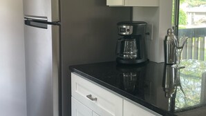 A kitchen with white cabinets, a stainless steel refrigerator, a coffee maker, and a glass decanter on the counter.
