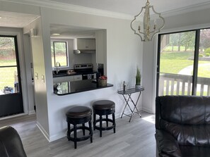 Enjoy a spacious living area with a kitchen, sofa, and potted plant, offering a view of the well-maintained lawn.