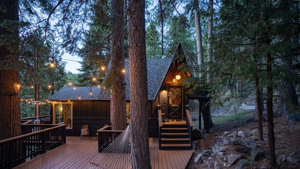 Una cabaña con terraza de madera, un pequeño porche y luces colgantes.
