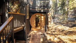 Una cabaña de madera con una escalera espiral que conduce a una terraza, rodeada de árboles.