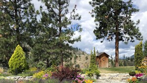 Un jardin avec un chalet en bois, un mur de pierre et une chaise au premier plan.