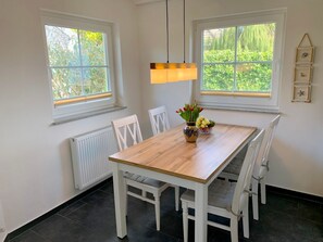 Ein Essbereich mit einem Holztisch, weißen Stühlen, einer Blumenvase und einer Obstschale.