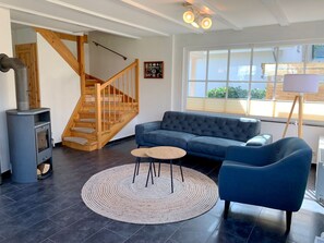 Ein modernes Wohnzimmer mit einem blauen Sofa, einem runden Teppich, einer Holztreppe und einem großen Fenster.