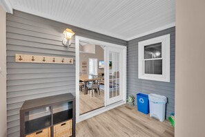 Une pièce aux murs gris, avec un plancher en bois, une porte-fenêtre coulissante donnant sur un coin repas, une petite table avec des chaises et une poubelle.