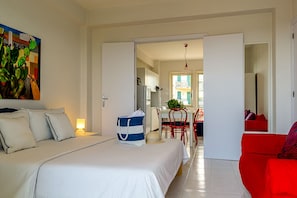 A hotel room with a bed, a red sofa, a dining area, and a kitchen visible through an open door. - The House Of Stefe - View of the gulf (Giardini Naxos)