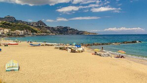 Una playa con barcos, sombrillas y un litoral rocoso.