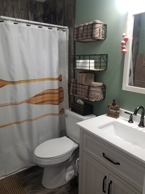 A bathroom with a shower curtain, toilet, sink, and shelves with towels.