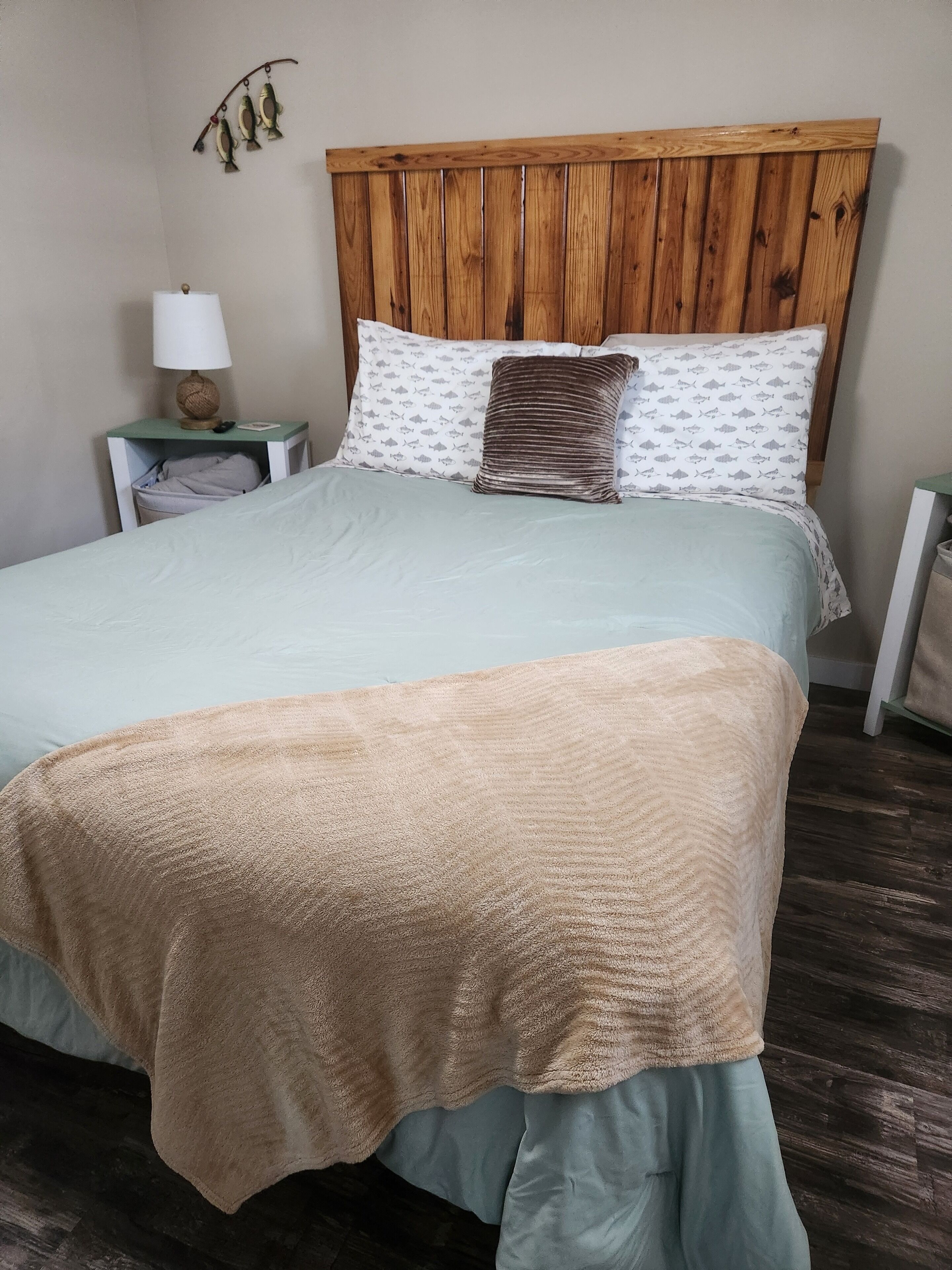 Ein Bett mit hölzernem Kopfteil, zwei Kissen mit Fischmotiven und ein Nachttisch mit Lampe.