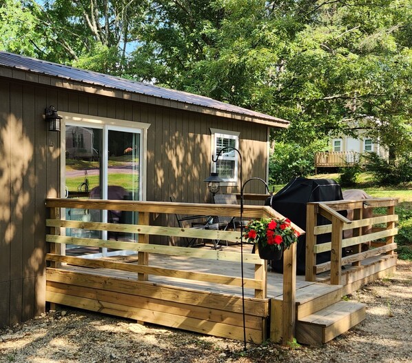 A wooden cabin with a porch, a grill, and a chair.
