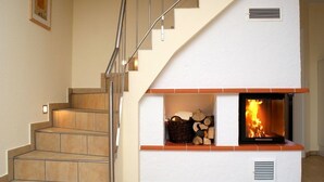Una escalera de diseño moderno, una chimenea con fuego y un cesto de leña.