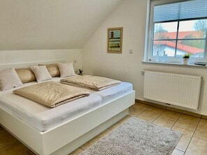 Un dormitorio con cama, ventana, radiador y un cuadro en la pared.