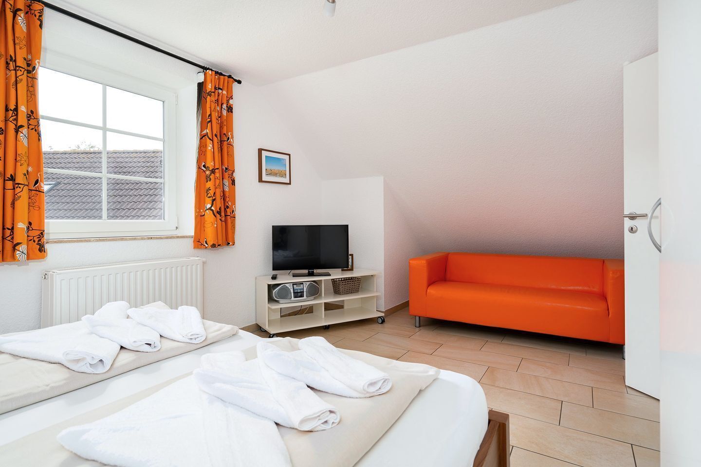Una habitación de hotel con cama, televisión, sofá y ventana con cortinas.