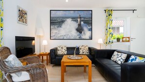 Una sala de estar con un sofá de cuero negro, una mesa de centro de madera, un televisor y un cuadro de un faro.