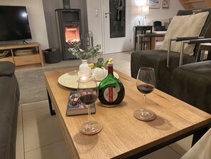 A cozy living room with a fireplace, a television, and a dining table set with a bottle of wine and glasses.