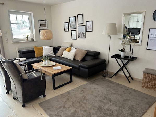 A modern living room with a black leather sofa, a wooden coffee table, a grey rug, and a large mirror.