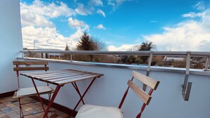 Un balcon avec une table et deux chaises, un sol carrelé et une vue sur le ciel et les bâtiments.