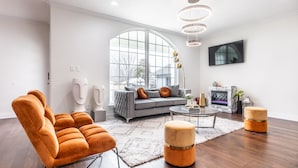 Een moderne woonkamer met een grijze bank, oranje fauteuils, een ronde salontafel en een open haard.