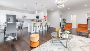Een moderne keuken met witte kastjes, een centraal eiland met barstoelen en een eethoek met grijze stoelen.