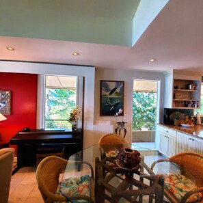 A modern kitchen with a dining area, featuring a glass-top table, wicker chairs, and a red accent wall.
