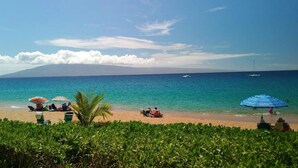 Ein Strand mit Sonnenschirmen, blauem Himmel und Booten im Wasser.