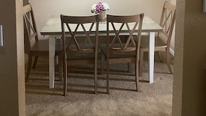 Uma sala de jantar com mesa, cadeiras, um quadro de uma praia e luminárias pendentes.