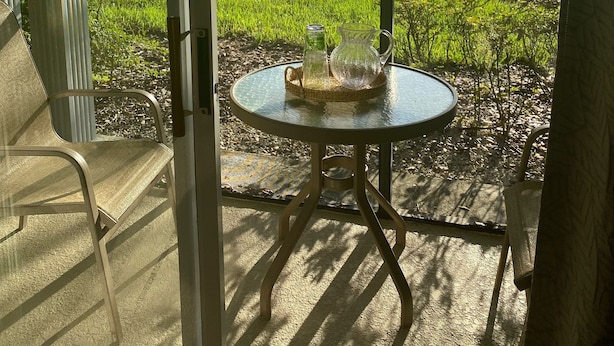 Porta de vidro que dá para um pátio com mesa, cadeiras e vista para um campo verde.