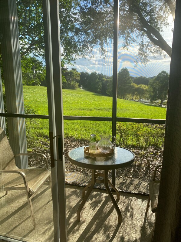 A glass door leading to a patio with a table, chairs, and a view of a green field.