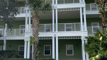 A two-story building with a green facade, white railings, and a central entrance.