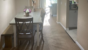 Uma área de jantar com uma mesa e cadeiras, um lustre e vista para a cozinha.