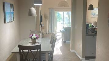 A dining area with a table and chairs, a hanging light fixture, and a view into the kitchen.