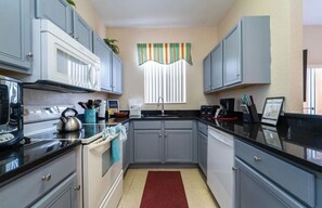 Compact kitchen with modern design, equipped with microwave, kettle, and kitchen utensils.